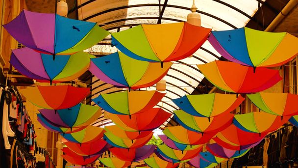 Bright umbrellas under the roof in the passage between two houses in the street of the old town. Urban architecture, decoration of the citys ancient streets in the city center - Photo, Image