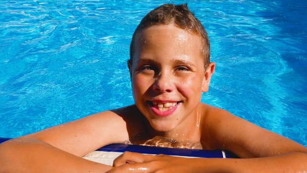 Egy boldog fiú úszik a medencében kék vízzel, felúszik az oldalára. Nyári vakáció a forró országokban. Nyaralni. Nyári vakáció a medencénél. Boldog családi vakációt! - Fotó, kép
