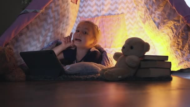 Akşam oynayan küçük kız tablette, çadırda çizgi film izliyor. Yüksek kaliteli FullHD görüntüler - Video, Çekim