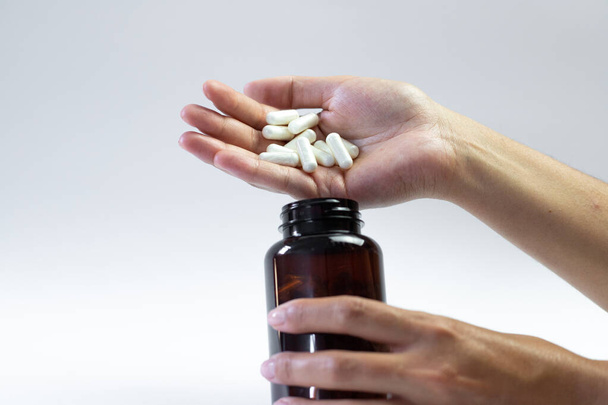Pilules de caféine sur fond blanc, main tenant un bocal avec des suppléments - Photo, image