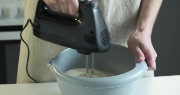 Großaufnahme eines kaukasischen Kochs, wie er in der Küche gekonnt Teig mit einem Mixer mixt. In eine Schürze gehüllt, erzeugen sein konzentrierter Blick und seine geschickten Hände ein faszinierendes Schauspiel kulinarischer Kunst. - Filmmaterial, Video