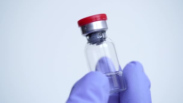 A kék orvosi kesztyűben lévő orvos kezéről készült közelkép üvegből készült injekciós üveg szérumot tartalmaz influenza, cukorbetegség, koronavírus, COVID-19, egyéb betegségek ellen. A vakcinázás fogalma, laboratóriumi kutatás.Új gyógyszerek feltalálása - Felvétel, videó