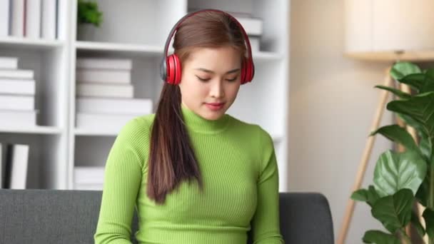 Young woman listening to music while relaxing on a sofa at home. Carefree, cheerful and happy female wearing headphones while enjoying a podcast and favorited song.. - Footage, Video