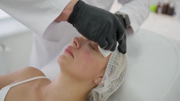 Una esteticista limpia la cara de una mujer con toallitas antibacterianas. Un médico haciendo un procedimiento de belleza en una clínica de cosmetología. Una esteticista que limpia la cara de un paciente en una clínica de belleza. - Metraje, vídeo