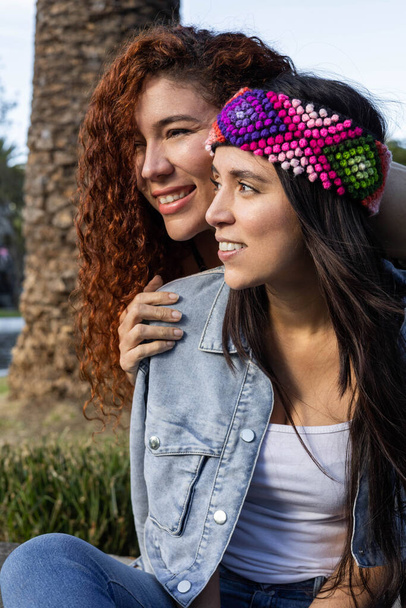 δύο Λατίνες γυναίκες, η μία με σγουρά μαλλιά και η άλλη με ίσια μαλλιά και πολύχρωμο κεφαλόδεσμο, νεανική μόδα σε ένα πάρκο με τη φύση, γυναικείο μοντέλο τρόπου ζωής - Φωτογραφία, εικόνα