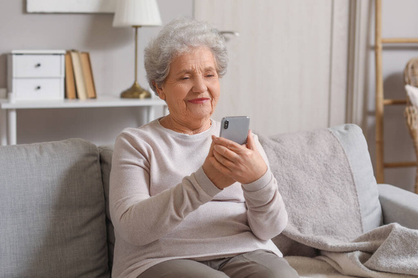 Donna anziana con cellulare video chat sul divano di casa - Foto, immagini