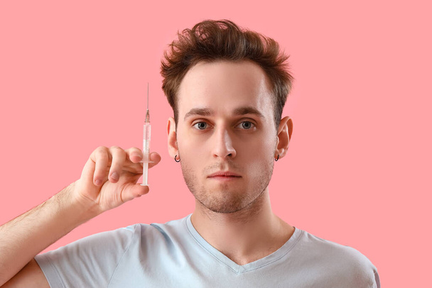Hombre joven con inyección para el crecimiento del cabello sobre fondo rosa, primer plano - Foto, imagen