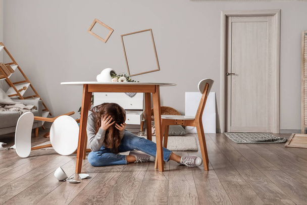 Mujer joven escondida debajo de la mesa de comedor durante el terremoto en casa - Foto, imagen