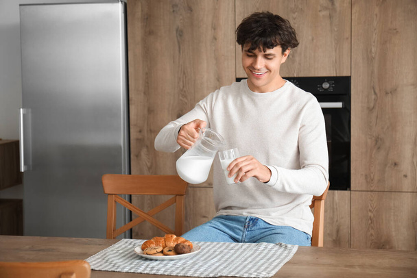 Young man drinking fresh milk in kitchen - Photo, Image