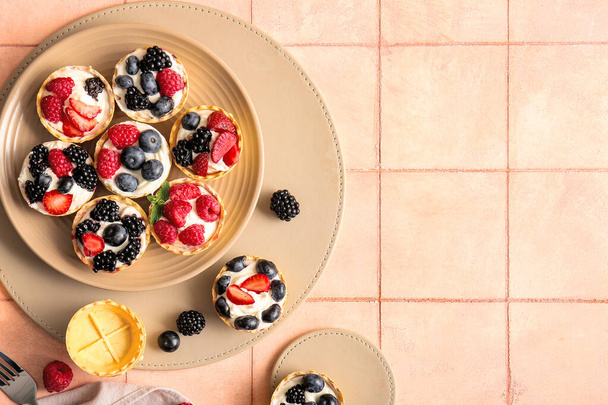 Plate of tasty tartlets with whipped cream and berries on pink tile background - Photo, Image