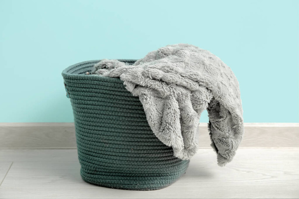 Basket with cozy blanket near blue wall, closeup - Photo, Image
