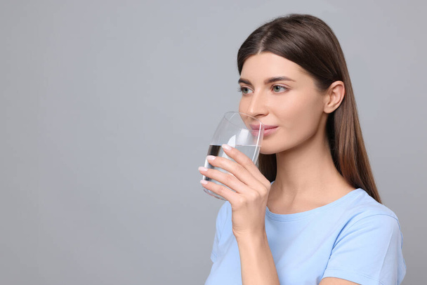 Healthy habit. Woman drinking fresh water from glass on grey background. Space for text - Zdjęcie, obraz