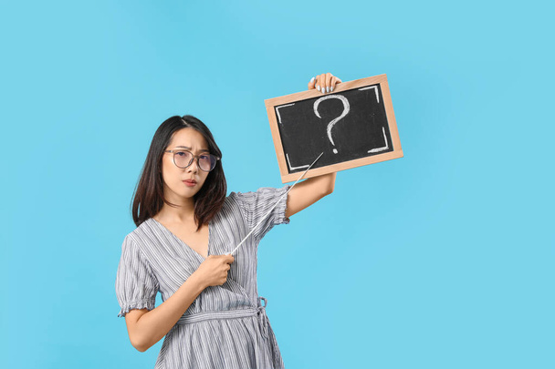 Upset Asian teacher pointing at chalkboard with question mark on blue background - Foto, immagini