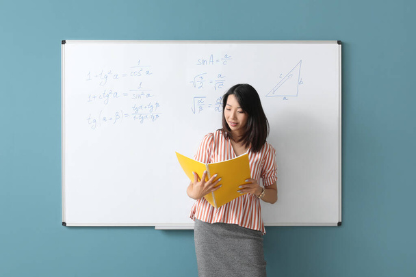 Profesor de matemáticas asiático con portátil cerca de flipboard en el aula - Foto, Imagen
