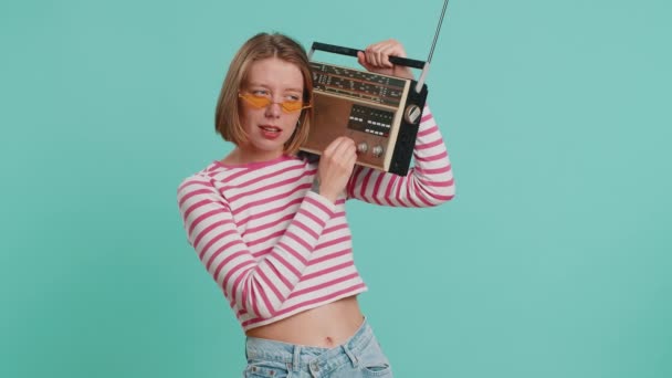 Woman in sunglasses using retro tape record player to listen music, disco dancing of favorite track, having fun, entertaining, fan of vintage technologies. Girl in crop top isolated on blue background - Footage, Video