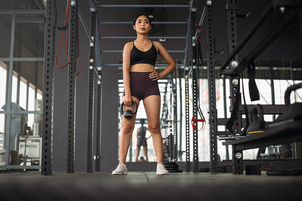 Güçlü Asyalı kadın spor salonunda kettlebell ile egzersiz yapıyor. Spor kıyafetleri giyen atlet kadın gri spor salonunda ağırlık ve halterli. Sağlıklı yaşam tarzı. - Fotoğraf, Görsel