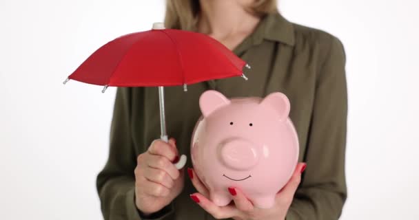 Financiële verzekering en veilig beleggingsconcept. Hand houdt rode paraplu over spaarvarken bank en beschermt geld - Video