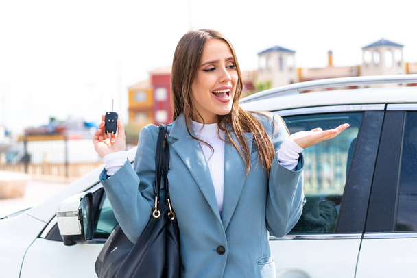 Junge hübsche Frau hält Autoschlüssel im Freien mit überraschendem Gesichtsausdruck - Foto, Bild