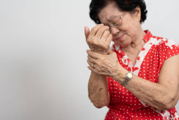 Пациентки пожилой азиатки страдают от онемения в руках от ревматоидного артрита. Старшая женщина массирует руку с болью в запястье. Концепция боли в суставах, ревматоидного артрита и проблем с рукой. - Фото, изображение