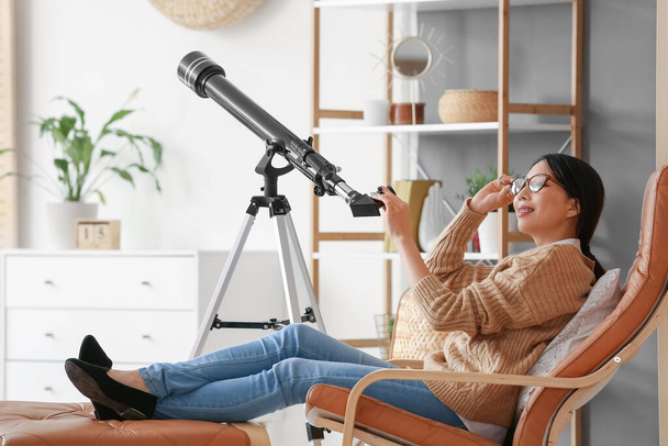 Genç Asyalı kadın evde teleskop kullanıyor. - Fotoğraf, Görsel
