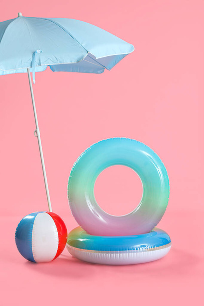 Pierścienie kąpielowe z piłką plażową i parasolem na różowym tle - Zdjęcie, obraz