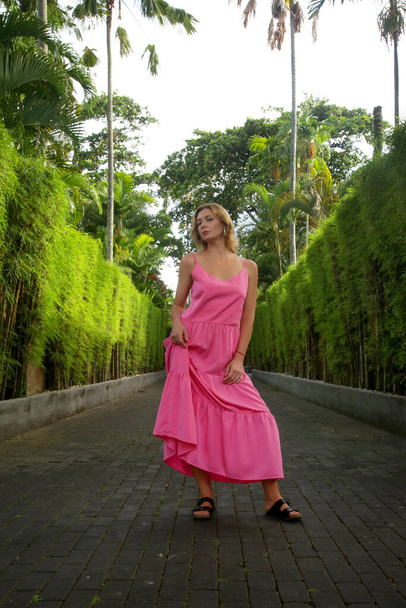 Outdoor portrait of stylish fashionable woman in bright pink dress in tropical resort. Natural light. Casual yet stylish summertime outfit, spring-summer fashion trend, tropical vacation style. - Photo, Image