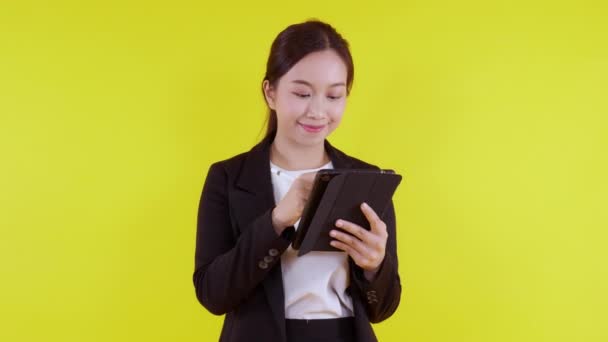 Портрет молодой азиатской бизнесвумен в костюме стоя с помощью планшетного компьютера записи в Интернет на желтом фоне, деловая женщина смотрит цифровой планшет с успехом, коммуникационная концепция. - Кадры, видео