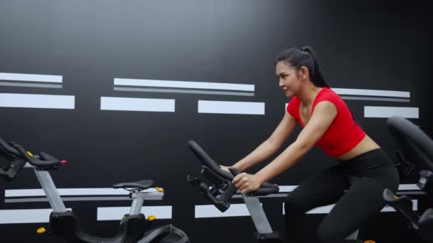 Молодая азиатка ездит на велосипеде машина для тренировки в фитнес-тренажерном зале, женский велоспорт для упражнений с мотивацией и концентрацией для благополучия и потери веса, спорта и здравоохранения. - Кадры, видео