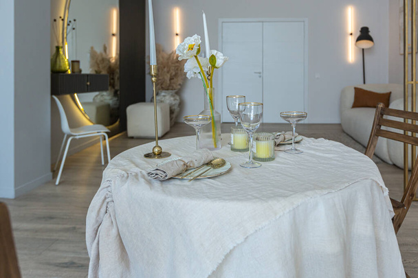 romantic table is served for two in the kitchen in a bright open-plan apartment in a modern style with light walls and wooden floors. - Foto, Imagem