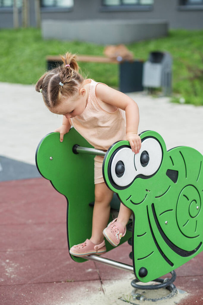 Rocking frog with spring for kids. Little toddler girl having fun at playground. Concept of kindergarten, baby development and early years - Photo, Image