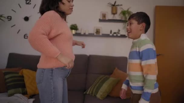 Latin young mother and son dance joyfully in living room at home on day off. Single mom enjoys company of her active child improvising party together at home. Happy family united in moments of leisure - Footage, Video