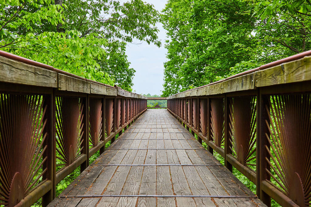 Immagine di Ponte con arrugginito modello di sole nascente su ringhiera con sentiero in legno usurato che porta a trascurare - Foto, immagini