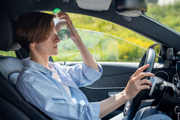 Kärsimys lämpö uupunut nainen kuljettaja istuu autossa avoin ikkuna laittaa kylmä pullo vettä otsaan liikenteessä. Ylikuumeneminen rypistynyt keski-ikä naisten kosketus ohjauspyörän kanssa silmät - Valokuva, kuva