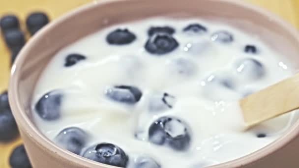 Houten lepel met yoghurt, bosbessen op houten ondergrond als ontbijt. Het eten van gezond voedsel, dieet, gewichtsverlies concept. Close-up, slow motion - Video