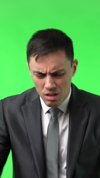 Tired young male manager with dark hair in formal outfit exhaling and wiping sweat from forehead after hard workday against chroma key - Footage, Video