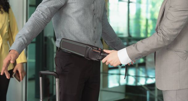 Sicherheitsbeamter mit einem Metalldetektor an einem männlichen Passagier am Flugsteig des Flughafens - Foto, Bild