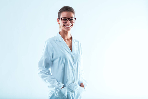 Woman in glasses, hair tied up, smiling with hands in her lab coat pockets. Specializing in science and technology, with internet and computers, has advanced her career. Intelligence, determination, a - Photo, Image