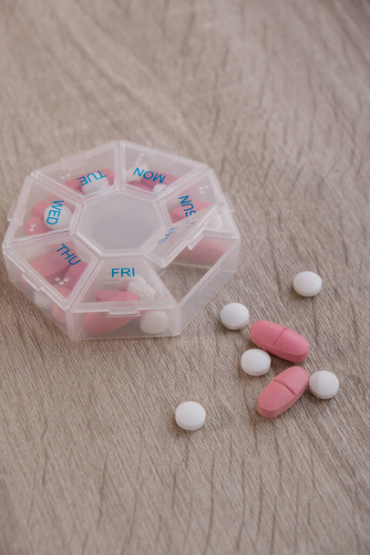 Organizer weekly shots Closeup of medical pill box with doses of tablets for daily take medicine with white pink drugs and capsules. Daily vitamins at home. Medication dietary supplements, immunity - 写真・画像
