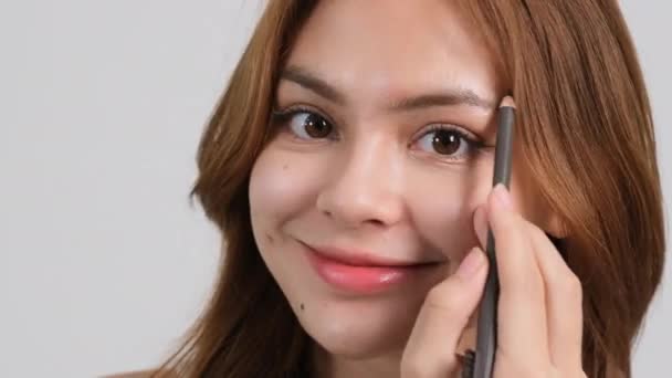 Young beautiful woman applying makeup her eyebrows for strong growth. looking at camera. - Footage, Video