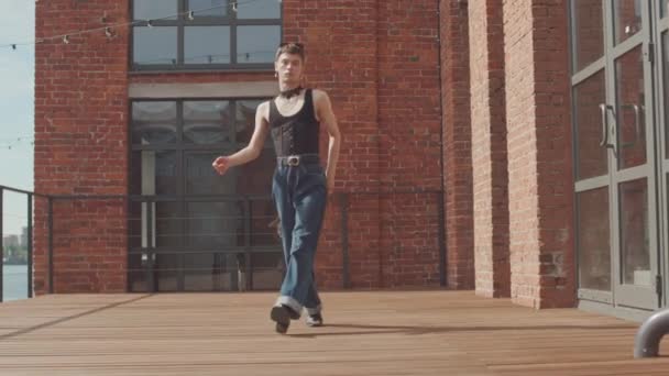 Teljes hosszúságú lassúság divatos fiú vintage kék farmer, fekete felső és masszív fojtogató a nyakán sétál felé kamera teljesítő vogue tánc mozog - Felvétel, videó