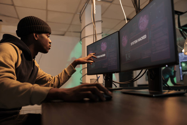 Pirata informático afroamericano plantación de virus de Troya para robar datos, mirando a los montores para crear malware. Persona que trabaja en spyware para irrumpir en el sistema y la red del gobierno, ciberataque. - Foto, imagen