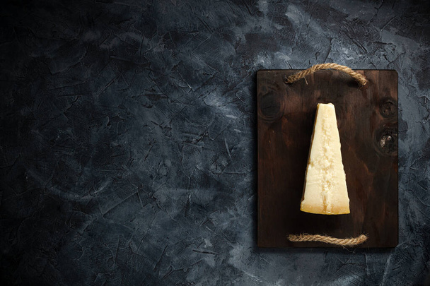 Вид сверху треугольного куска твердого сыра на деревянной разделочной доске - Фото, изображение