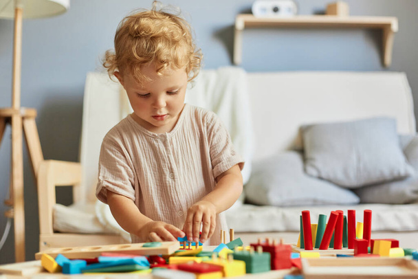 Colorful learning toys. Building blocks fun. Playful daycare activities. Childhood development games. Little blonde baby girl palying with wooden sorter toys at home interior. - 写真・画像