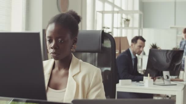 Genç Afrikalı Amerikalı kadın programcının orta yavaş portresi. Kameraya gülümsüyor. Çalışma masasında bilgisayar monitörünün önünde oturuyor. - Video, Çekim