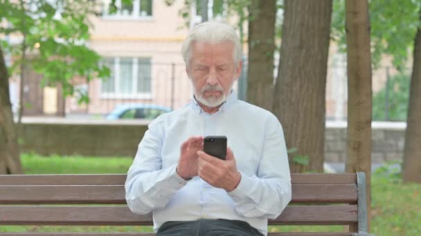 Droevige senior oude man met Online Loss op Smartphone tijdens het zitten op een bank - Video