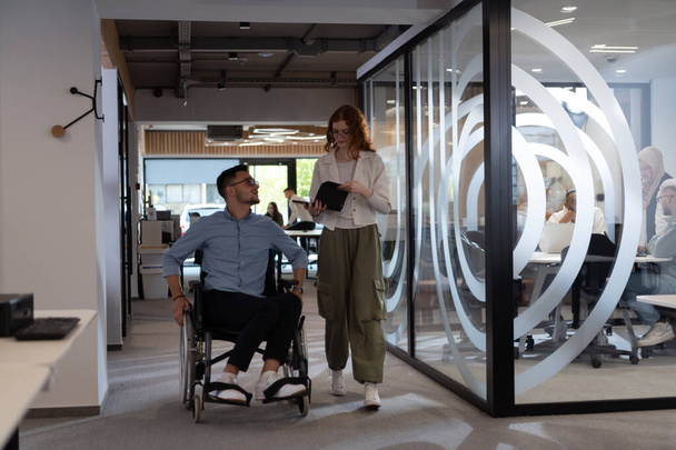 Young business colleagues, collaborative business colleagues, including a person in a wheelchair, walk past a modern glass office corridor, illustrating diversity, teamwork and empowerment in the - Foto, immagini
