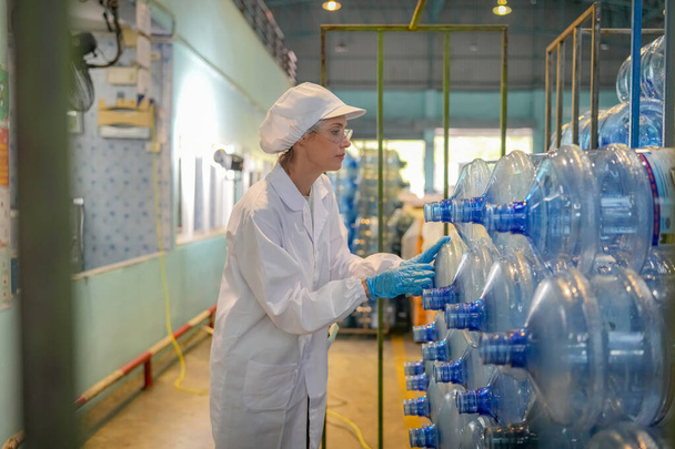 Kobieta pracująca w systemie odwróconej osmozy dla elektrowni. RO system dla przemysłu, urządzenia, które są popularne do instalacji z rurami w przemysłowych takich chemikaliów, elektrowni, ropy naftowej i gazu. Młoda szczęśliwa pracownica w rozlewni sprawdzająca butelki wody - Zdjęcie, obraz