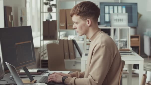 Slowmo muotokuva nuori valkoihoinen mies ohjelmoija hymyilee kameralle, kun koodaus tietokoneella on kirkas moderni IT-toimisto - Materiaali, video
