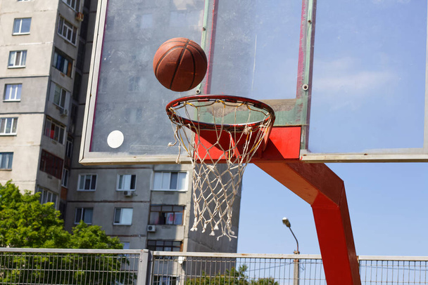 Μπάσκετ μπάλα πετά στο δαχτυλίδι στο γήπεδο του δρόμου αθλητικών - Φωτογραφία, εικόνα