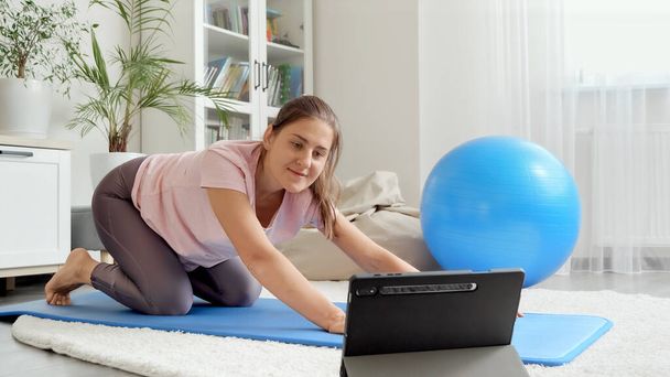 Boldog mosolygós nő integetett neki online sportrs edzés közben nézi fitness leckét tabletta számítógépen. Az egészségügyi ellátás, a sport és a jóga fogalma otthon - Fotó, kép